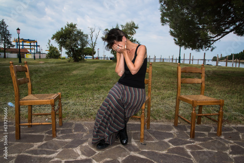 Una donna triste piange disperata seduta su una sedia di legno in un giardino