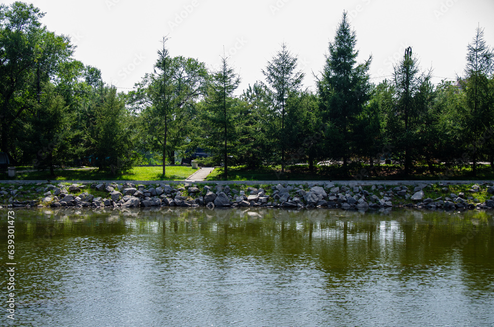 A pond surrounded by a monument and green trees with a lawn A pond surrounded by a monument and green trees with a lawn