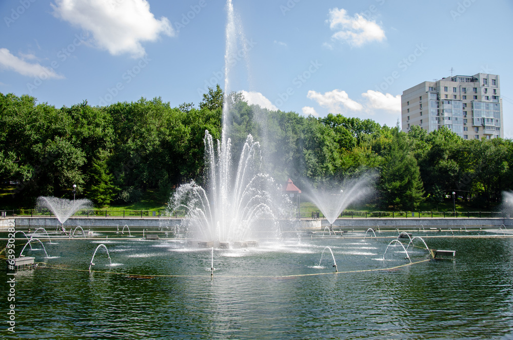 Fototapeta premium A pond with working fountains, surrounded by a monument of trees and lawn