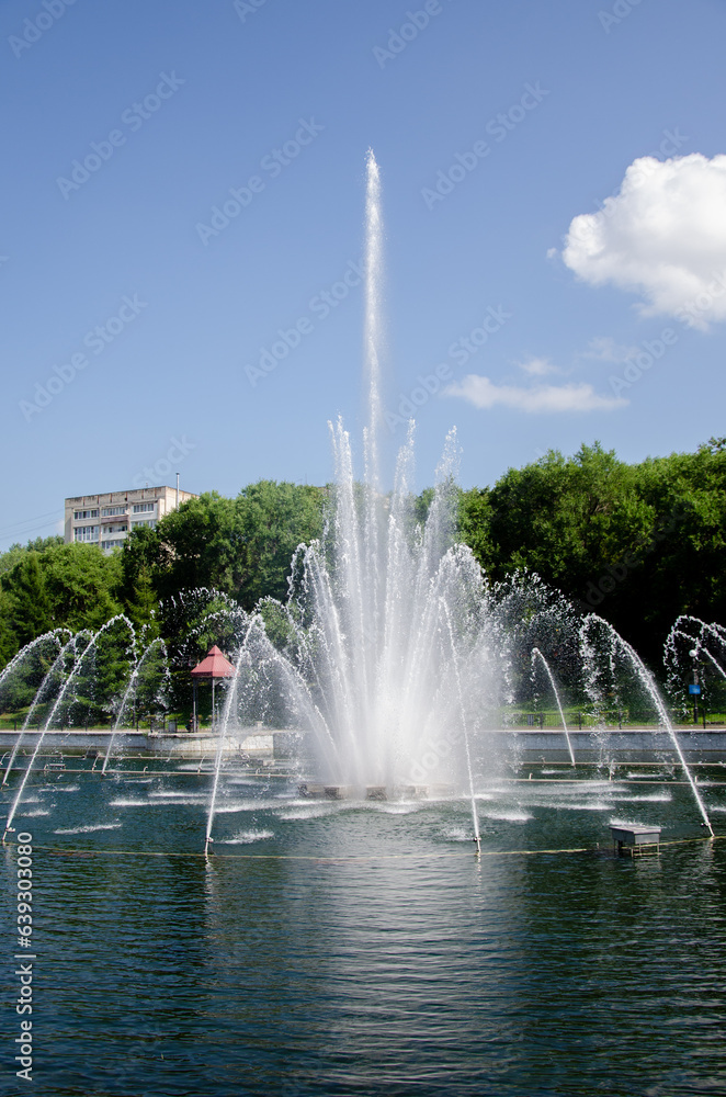 A pond with working fountains, surrounded by a monument of trees and lawn A pond with working fountains, surrounded by a monument of trees and lawn