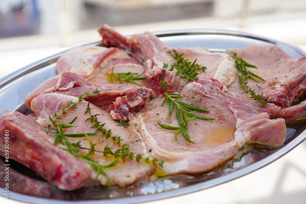 Closeup of Fresh raw pork chops bone steak with rosemary, thyme and olive oil on a silver tray