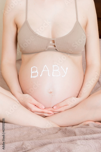 Wallpaper Mural a pregnant girl sits at home on the bed and smears an anti-stretch mark cream on her stomach. Pregnancy, motherhood, preparation and expectation concept. the word baby on the belly Torontodigital.ca