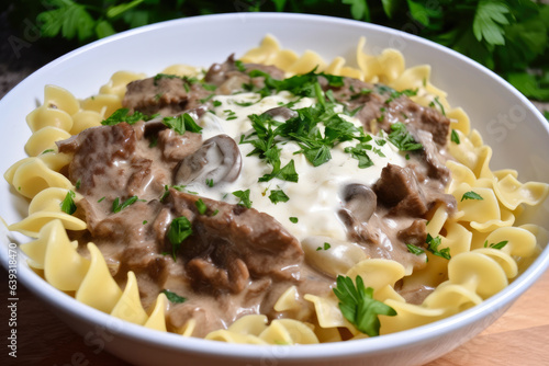 A white porcelain bowl holds a steaming hot beef stroganoff, topped with a dollop of sour cream and a sprinkle of parsley for added flavor