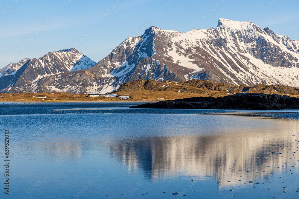 mountains with reflection at a beach of a fiord in lofoten norway in winter