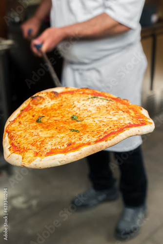 A chef takes a hot 4-cheese pizza out of the oven, holding it on a special baking peel