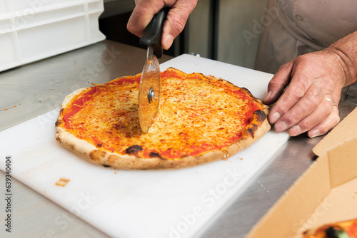 The chef cuts a hot 4-cheese pizza just out of the hot oven