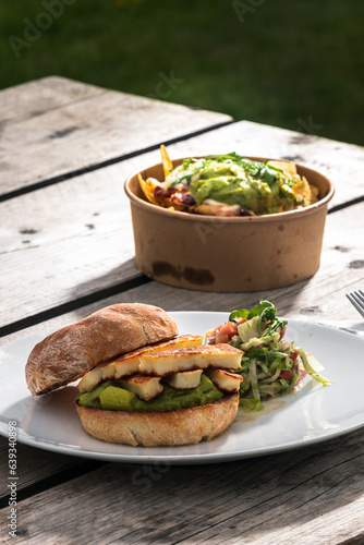 A burger and a salad on a white plate at an outdoor café on a wooden table, clean cutlery and napkin