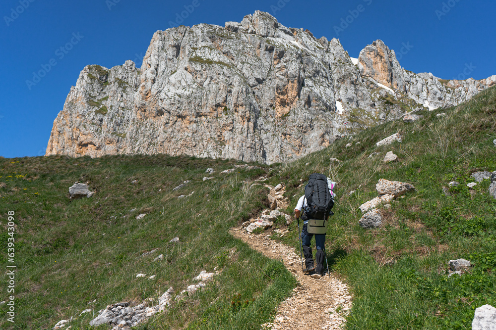 A tourist with a backpack walks along a path in the mountains.