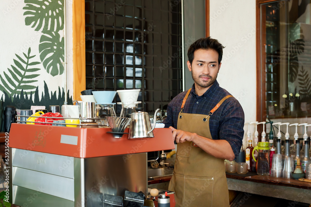Fototapeta premium Portrait Nice-looking Asian man wh owns shop wearing apron, man standing making coffee according order that customer ordered standing in front coffee machine that can do all coffee menu...