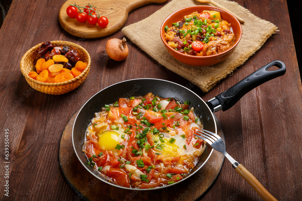 Jewish food hot cholent and shakshuka in a frying pan on a set Shabbat table. Jewish food hot cholent and shakshuka in a frying pan on a set Shabbat table.