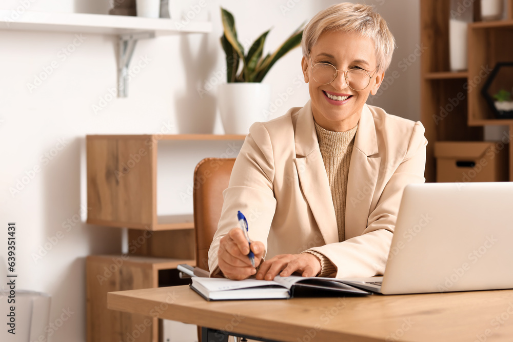 Mature businesswoman writing at table in office Mature businesswoman writing at table in office