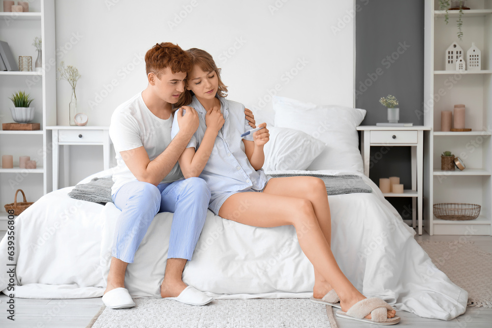 Sad young couple with pregnancy test in bedroom Sad young couple with pregnancy test in bedroom