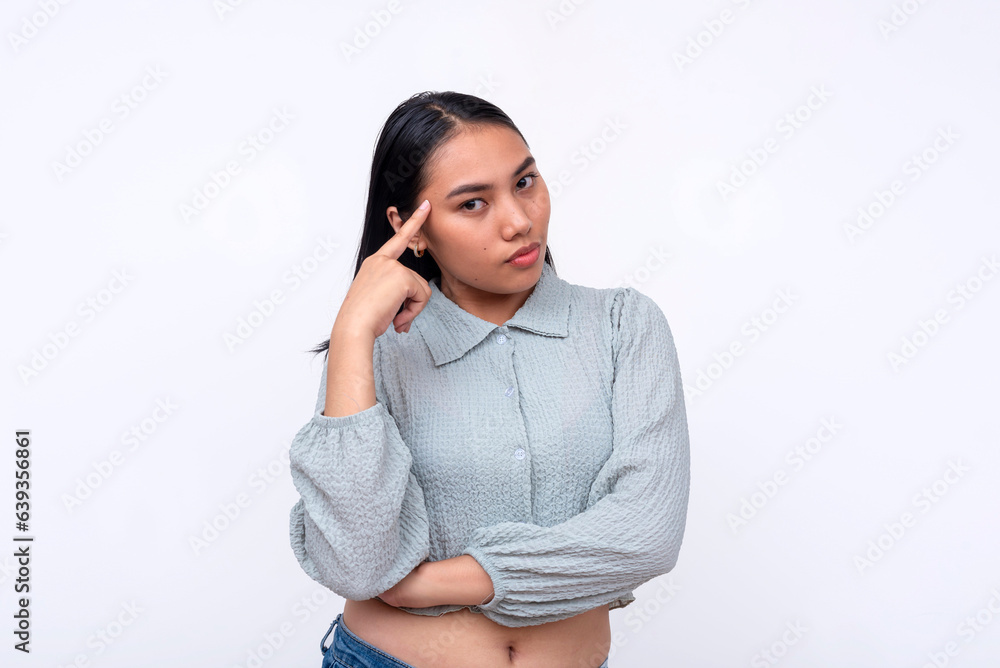 A young serious asian woman pointing to her temple. Looking at someone telling them she is aware of their actions, proclaiming her smarts. Isolated on a white background. A young serious asian woman pointing to her temple. Looking at someone telling them she is aware of their actions, proclaiming her smarts. Isolated on a white background.