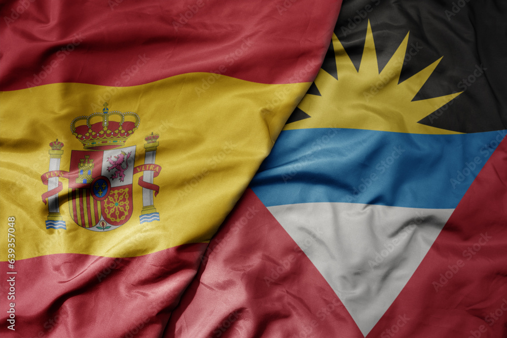big waving national colorful flag of spain and national flag of antigua and barbuda .