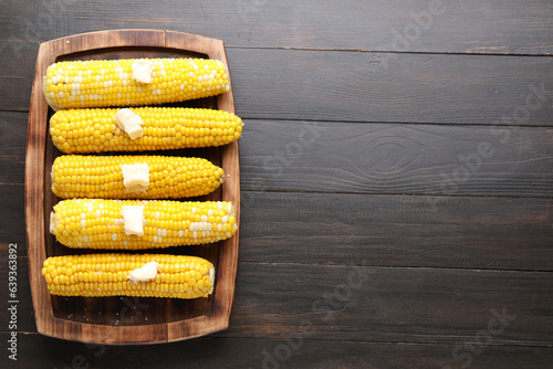 Board of boiled corn cobs with butter on wooden background photo