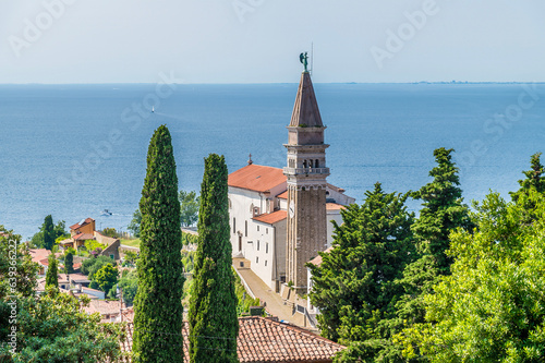 Schilderij op canvas A view past trees towards the cathedral in the town of Piran, Slovenia in summer