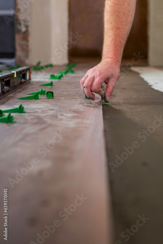Close up hands of repairman laying tiles with tile leveling system on the floor in a new house
