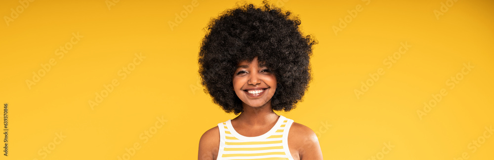 Studio portrait of happy young woman with afro hairstyle looking and smiling to the camera. Joyful girl posing on yellow vibrant background Studio portrait of happy young woman with afro hairstyle looking and smiling to the camera. Joyful girl posing on yellow vibrant background
