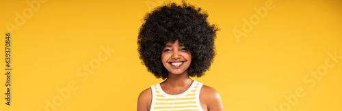 Studio portrait of happy young woman with afro hairstyle looking and smiling to the camera. Joyful girl posing on yellow vibrant background