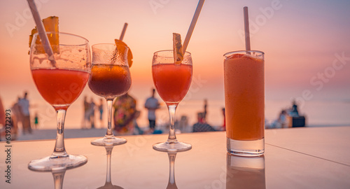 Colorful drinks in bar with blur beach party people and colorful sunset sea sky in background. Luxury outdoors leisure lifestyle, relaxation and romantic colors, blurred people partying summer evening
