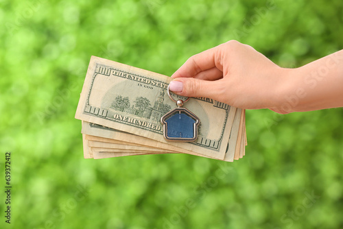 Vászonkép Female hand holding trinket in house shape and money on decorative green grass background