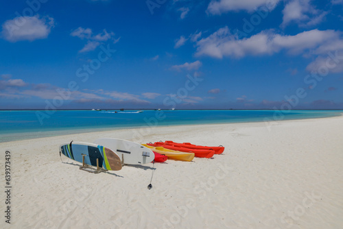 Beach coast in Maldives sea. Sup boards, kayaks close zo calm ocean bay water. Outdoor sport recreational equipment, fun wellbeing water activity. Sunshine, blue seascape sky, tropical resort
