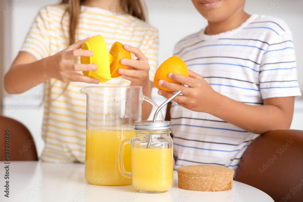 Little children making fresh orange juice at table in kitchen Little children making fresh orange juice at table in kitchen