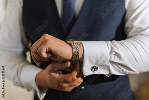A man's watch in his hands. A man adjusts and puts on a watch on his wrist. The groom is preparing for the wedding