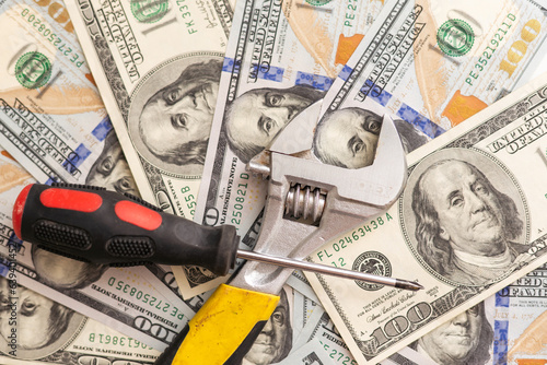 Tools lying over 100 dollars banknotes background. Pliers and screwdriver against US money. Correction, adjustment and improvement of budget concept. Copyspace photo