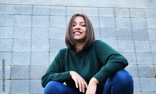 Mujer feliz y sonriente frente a una pared de color gris.