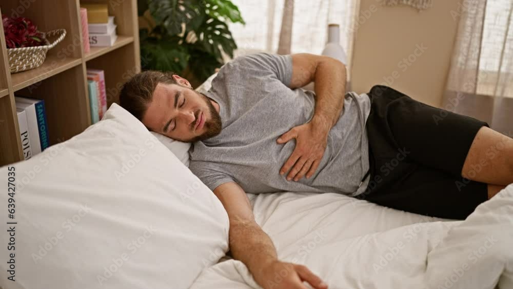 Young hispanic man suffering for stomach ache lying on bed at bedroom Young hispanic man suffering for stomach ache lying on bed at bedroom