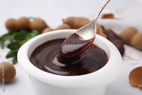 Taking tasty tamarind sauce with spoon from bowl on table, closeup