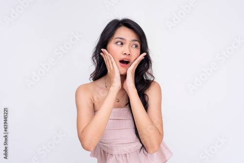 A surprised young asian woman gasps in amazement, both hands placed on her cheeks. A startling revelation. Isolated on a white background.