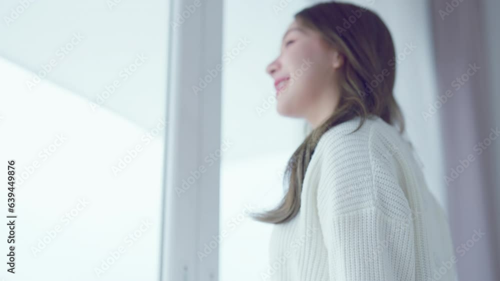 Young asian woman standing looking out of window in house or hotel room, opening curtains in the morning enjoying sunlight feeling happy Young asian woman standing looking out of window in house or hotel room, opening curtains in the morning enjoying sunlight feeling happy
