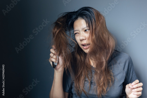 Asian girl with a comb and problem hair on gray background. Asian young woman holding brush, hairbrush with long loss hair problem after brushing.