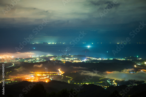 Brightly lit Taipei city night scene with dynamic clouds in the sky. The Wufenshan Weather Radar Station stands on the top of the mountain. Taiwan
