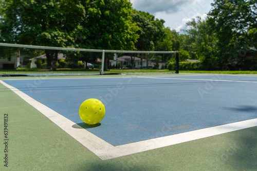 Recreational sport of pickleball court and ball in the United States with green and blue court with yellow ball on line. © KingmaPhotos