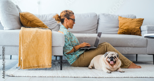 Domestic lifestyle people and animal together in friendship and life. One woman working on laptop sitting on the carpet at home with best friend dog relaxing near. Living room interior. Leisure.