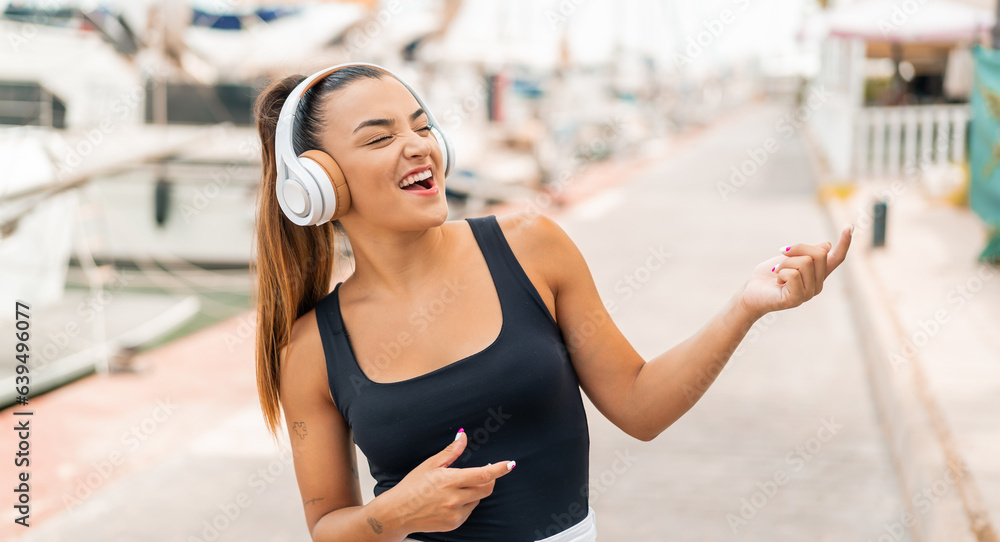 Young pretty woman at outdoors listening music and doing guitar gesture