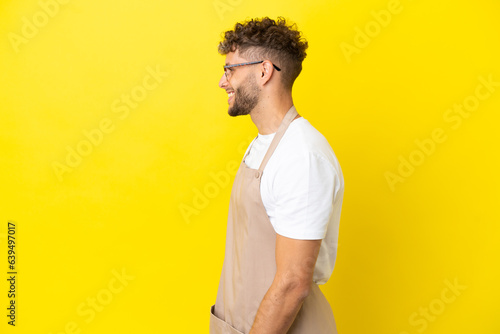 Restaurant waiter blonde man isolated on yellow background laughing in lateral position