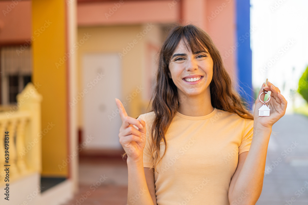 Young woman holding home keys at outdoors pointing up a great idea Young woman holding home keys at outdoors pointing up a great idea