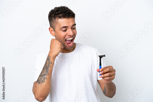 Young Brazilian man shaving his beard isolated on white background celebrating a victory