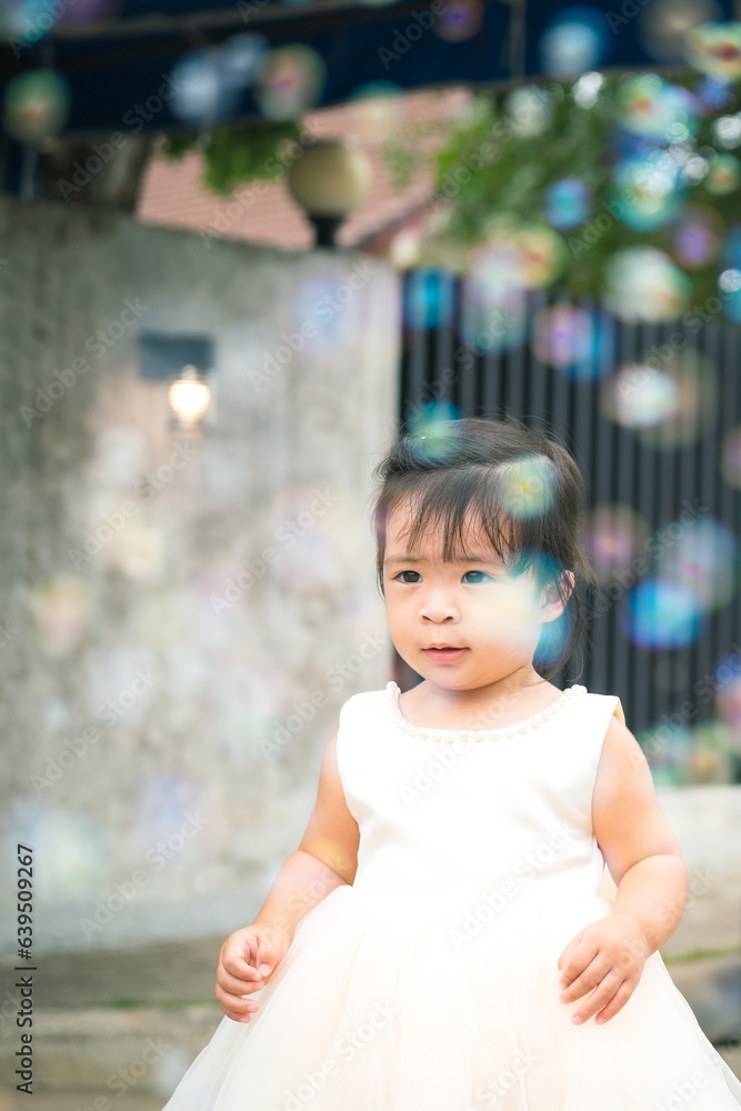Naklejka premium A cute little girl is white dress during playing air soap bubble with happiness action in the wedding event. Girl portrait photo, face focus.