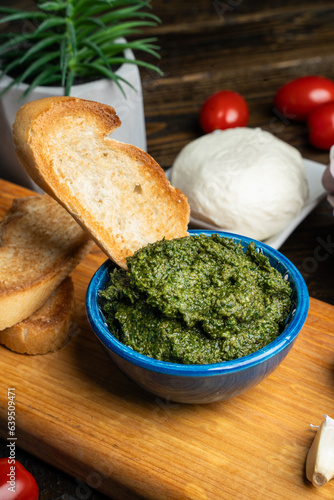 Traditional Italian pesto sauce served with mozzarella cheese, tomatoes and bruschetta on a dark wooden table