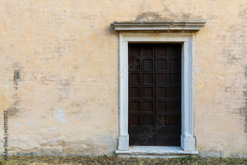 Vecchia porta di legno sulla parete gialla con erba in primo piano. © snake_xenzia