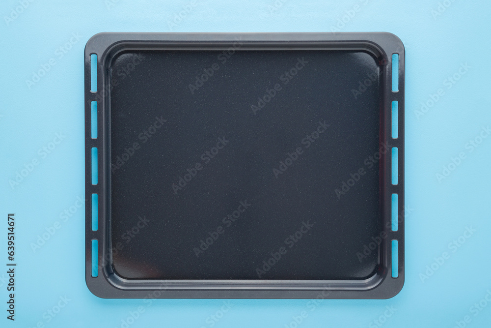 Empty new dark black oven tray on light blue table background. Pastel color. Closeup. Top down view. Empty new dark black oven tray on light blue table background. Pastel color. Closeup. Top down view.