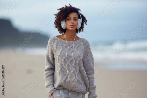 Confused Sad Indignant African Woman Wear Knitted Sweater Headphones Walking On The Beach Background . Сoncept African Femininity, Mental Health Awareness, Representation Of Women Of Color