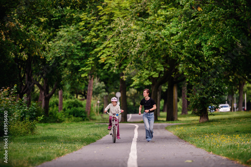 Wallpaper Mural Young mother in jeans and black t-shirt teaching and playing with her daughter in summer parks while girl riding a bike Torontodigital.ca