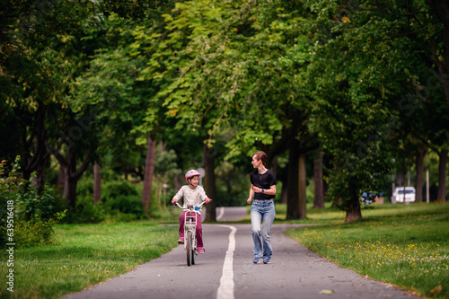 Wallpaper Mural Young mother in jeans and black t-shirt teaching and playing with her daughter in summer parks while girl riding a bike Torontodigital.ca