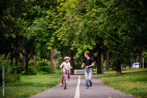 Wallpaper Mural Young mother in jeans and black t-shirt teaching and playing with her daughter in summer parks while girl riding a bike Torontodigital.ca